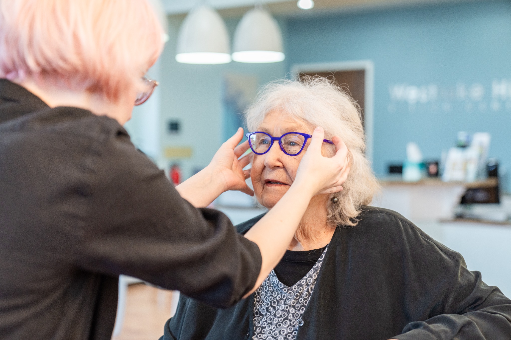 A Bright Side Optical team member carefully checking blue eyeglass frames on a seated client