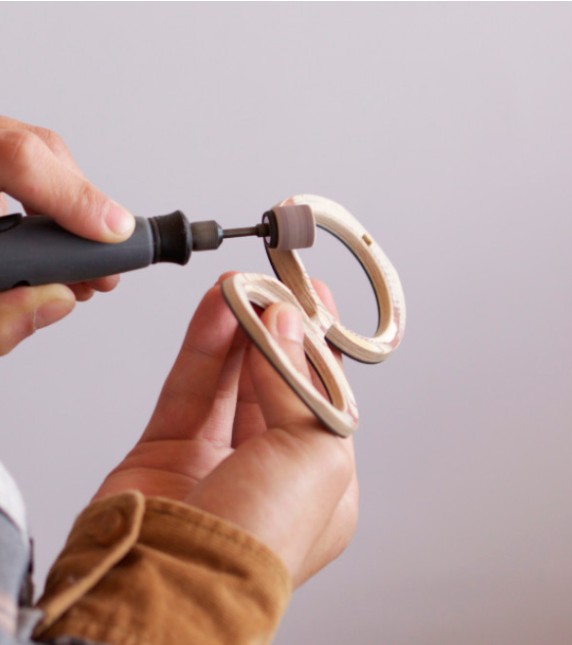 Hands carefully finishing the curved inside edge of a Nina Mûr wooden frame with a rotary tool