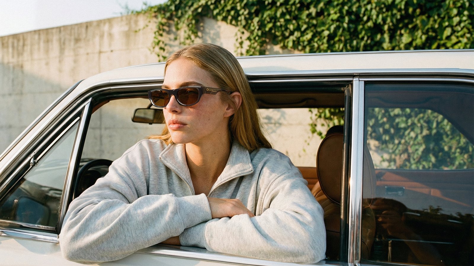 UniqueDesignMilano Passport campaign showing a woman wearing sculptural dark sunglasses beside a vintage car