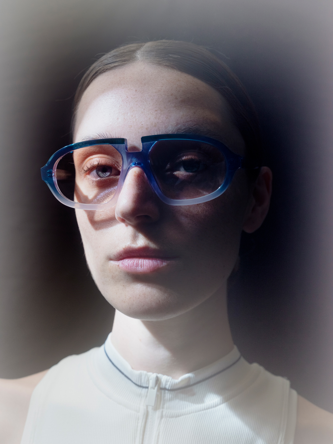 Official Veronika Wildgruber campaign portrait of a woman wearing sculptural blue translucent glasses with a lifted brow and a white sleeveless top